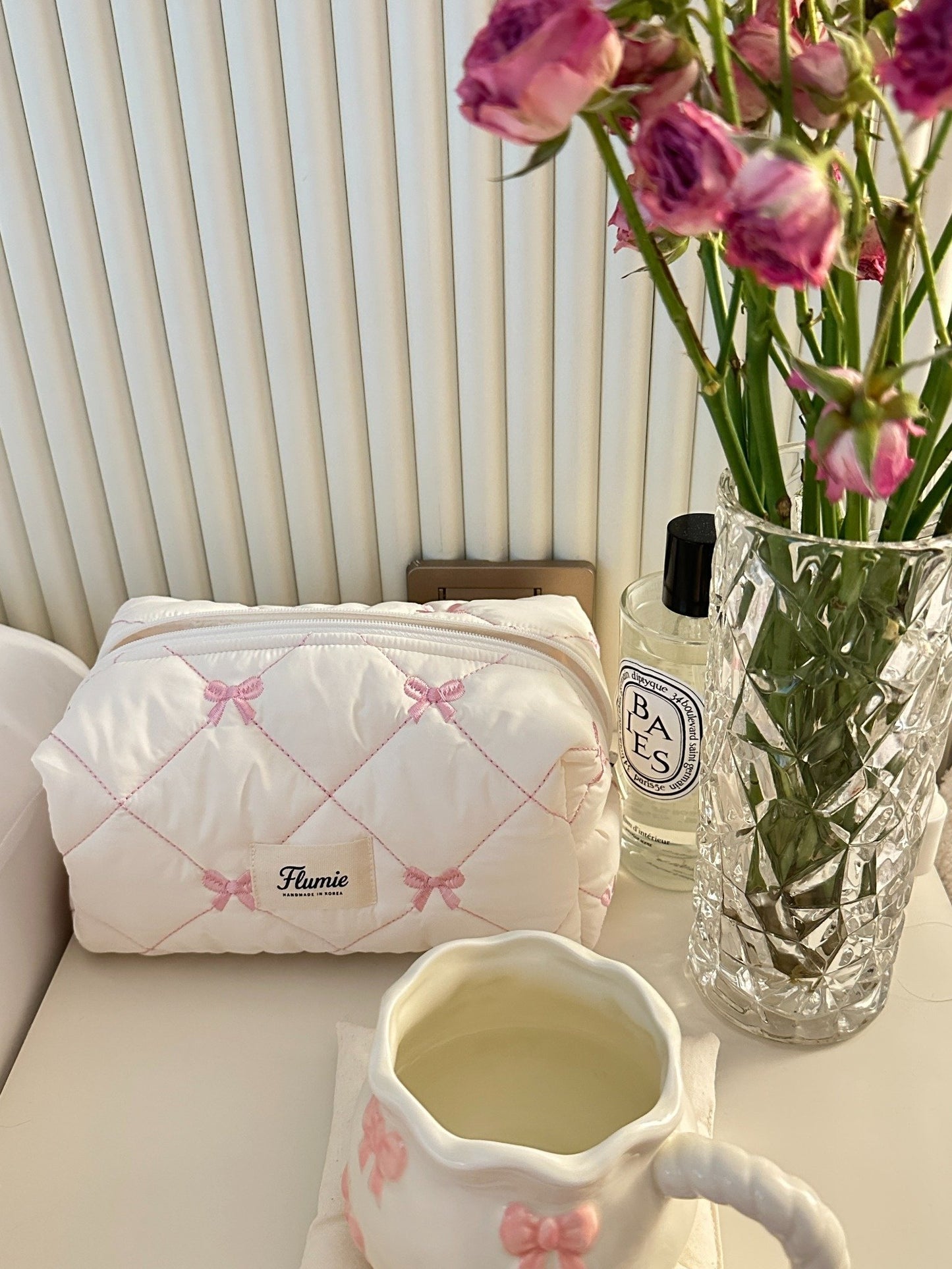 Ivory bow quilted pouch styled with flowers, Diptyque perfume, and teacup