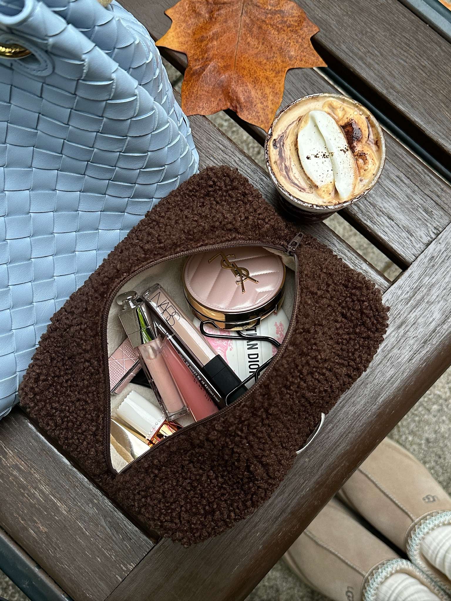 Open pouch filled with makeup essentials, set beside cozy textures and warm seasonal tones