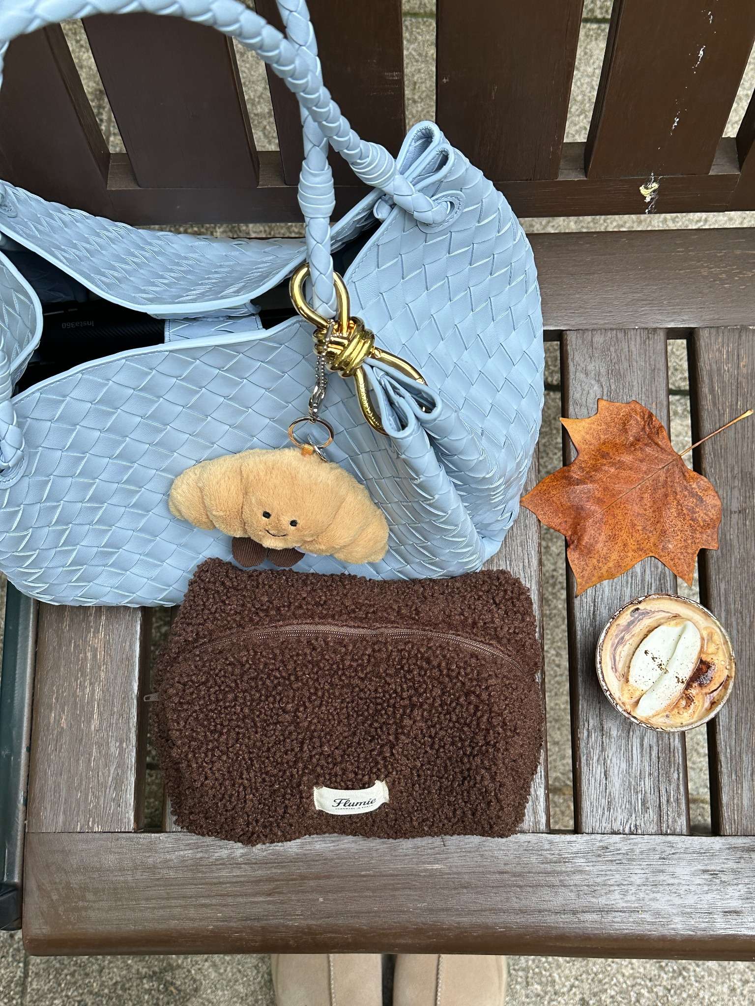 Cocoa fluffy pouch styled with a blue woven bag, maple leaf and latte, evoking a soft autumn café mood