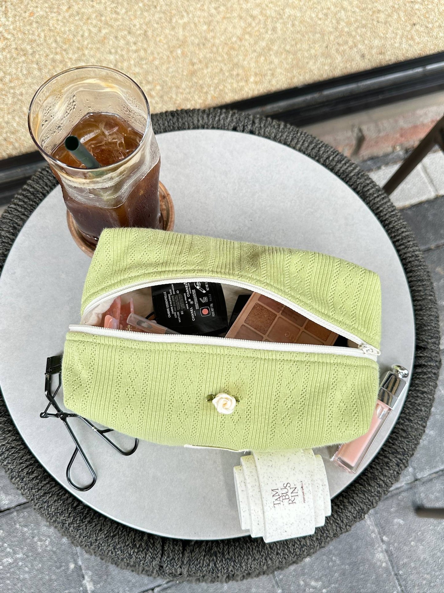 Matcha latte pouch with makeup essentials and iced coffee, capturing a relaxed clean girl moment at a café
