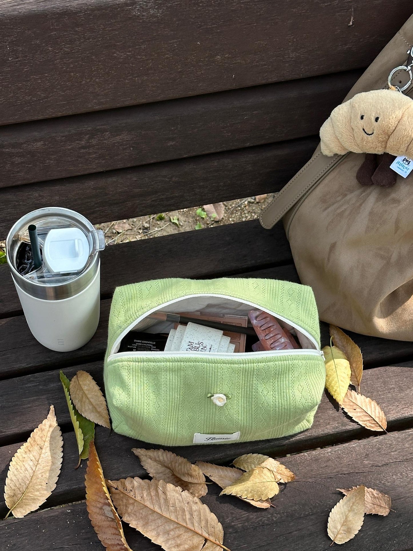 Creamy green pouch nestled among fallen leaves and coffee tumbler, bringing soft fall vibes to your outdoor moments