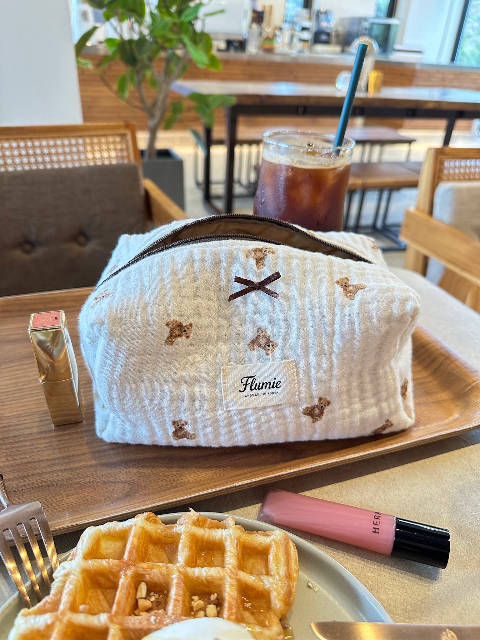 Flumie teddy bear pouch styled with iced coffee and waffles, creating a warm and cozy café mood